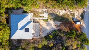 An aerial view of a house with a sloped roof, a paved driveway, and a parked car. - Seas The Day - Brand New Villa W/ocean View, Walk To Rainbow Bea 3 Bedroom Home (Rainbow Bay)
