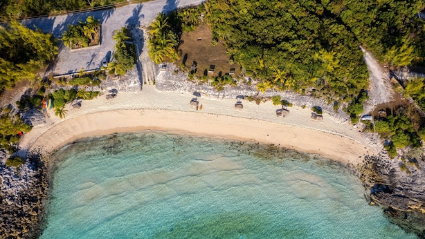 An aerial view of a beach with clear turquoise waters, a sandy shore, and several small structures along the beach. - Seas The Day - Brand New Villa W/ocean View, Walk To Rainbow Bea 3 Bedroom Home (Rainbow Bay)
