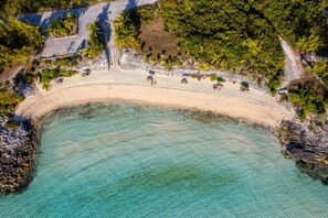 Luchtbeeld van een strand met helder turquoise water, een zandstrand en verschillende kleine gebouwen langs de kust.