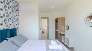 Une chambre d’hôtel moderne, équipée d’un lit, d’une armoire, d’un bureau et d’une salle de bain visible à travers une porte ouverte.