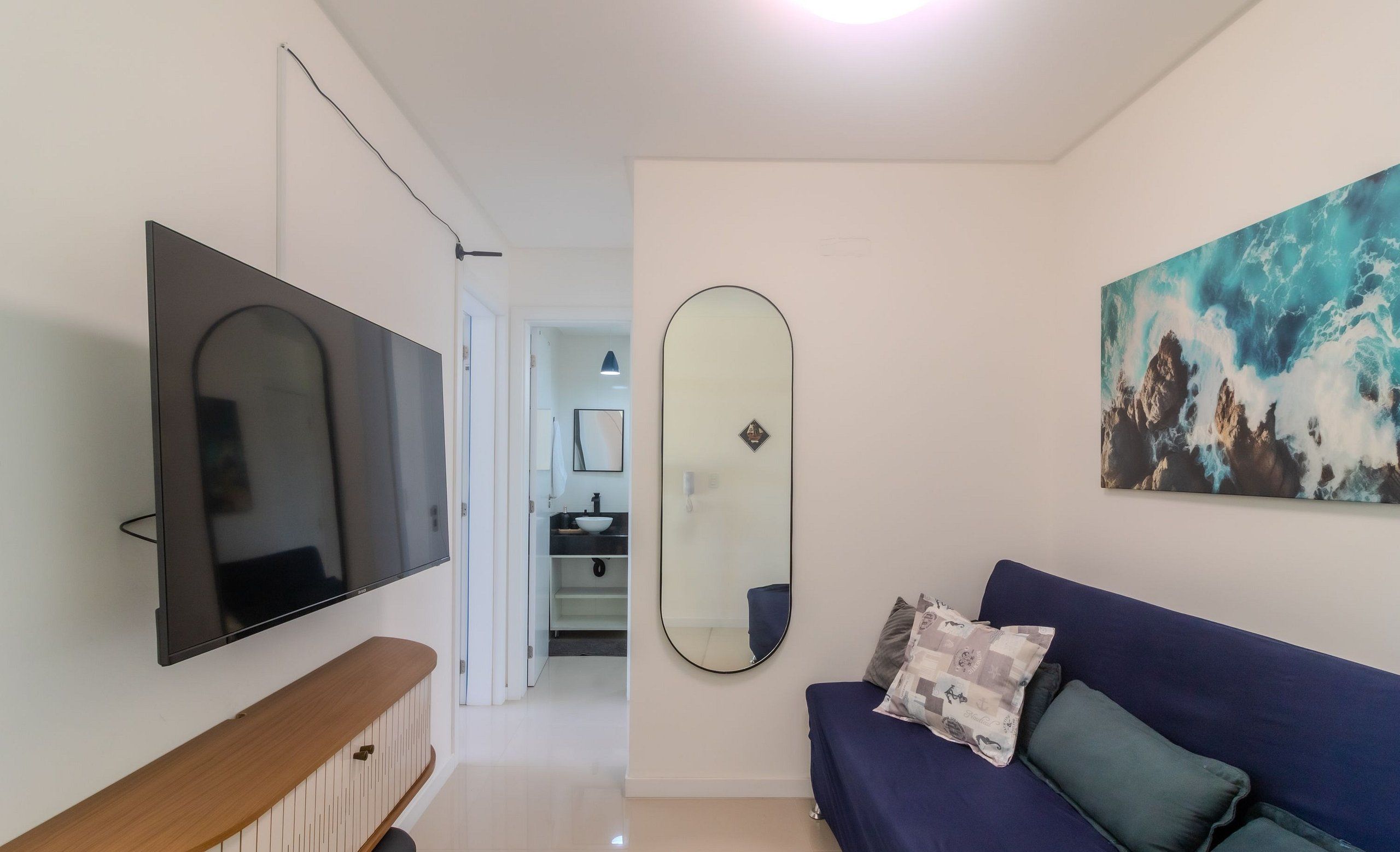 Una sala de estar moderna con un televisor de pantalla plana, un sofá con cojines, un espejo grande y un cuadro en la pared.