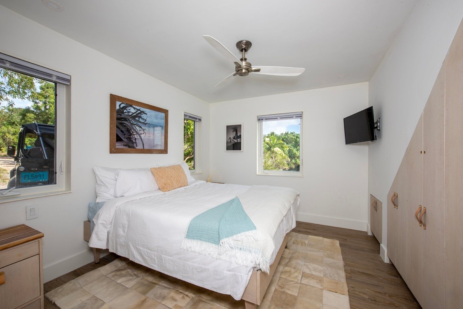 Une chambre à coucher avec un lit, un ventilateur de plafond, une télévision et des fenêtres donnant sur un paysage verdoyant.