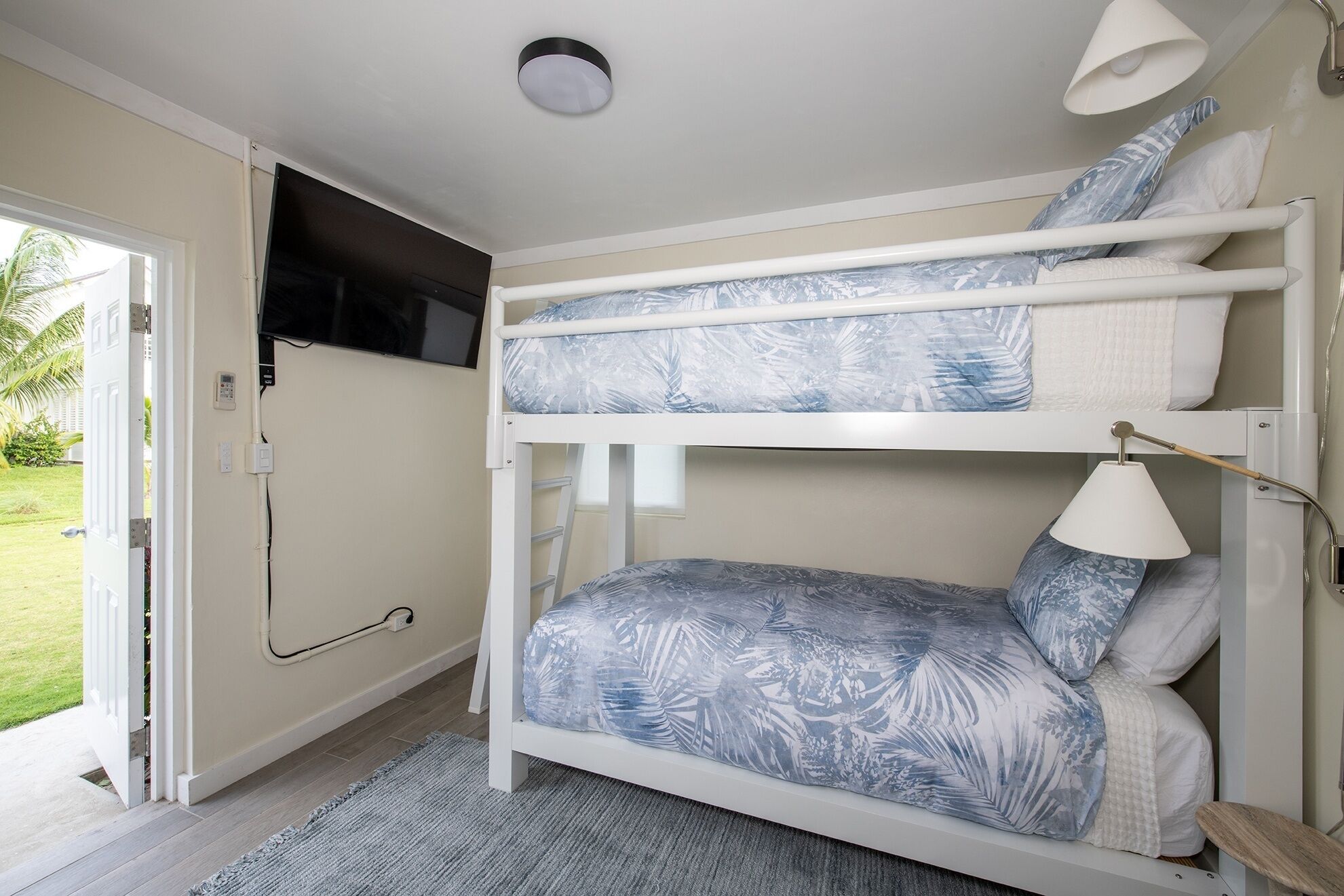 Una cama litera con un televisor montado en la pared, un enchufe y una puerta que da a un balcón.