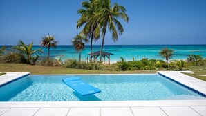 A swimming pool with clear blue water, surrounded by palm trees and a view of the ocean. - Cricket Beach House-luxurious Beachfront House 5 Bedroom Home (North Palmetto Point)
