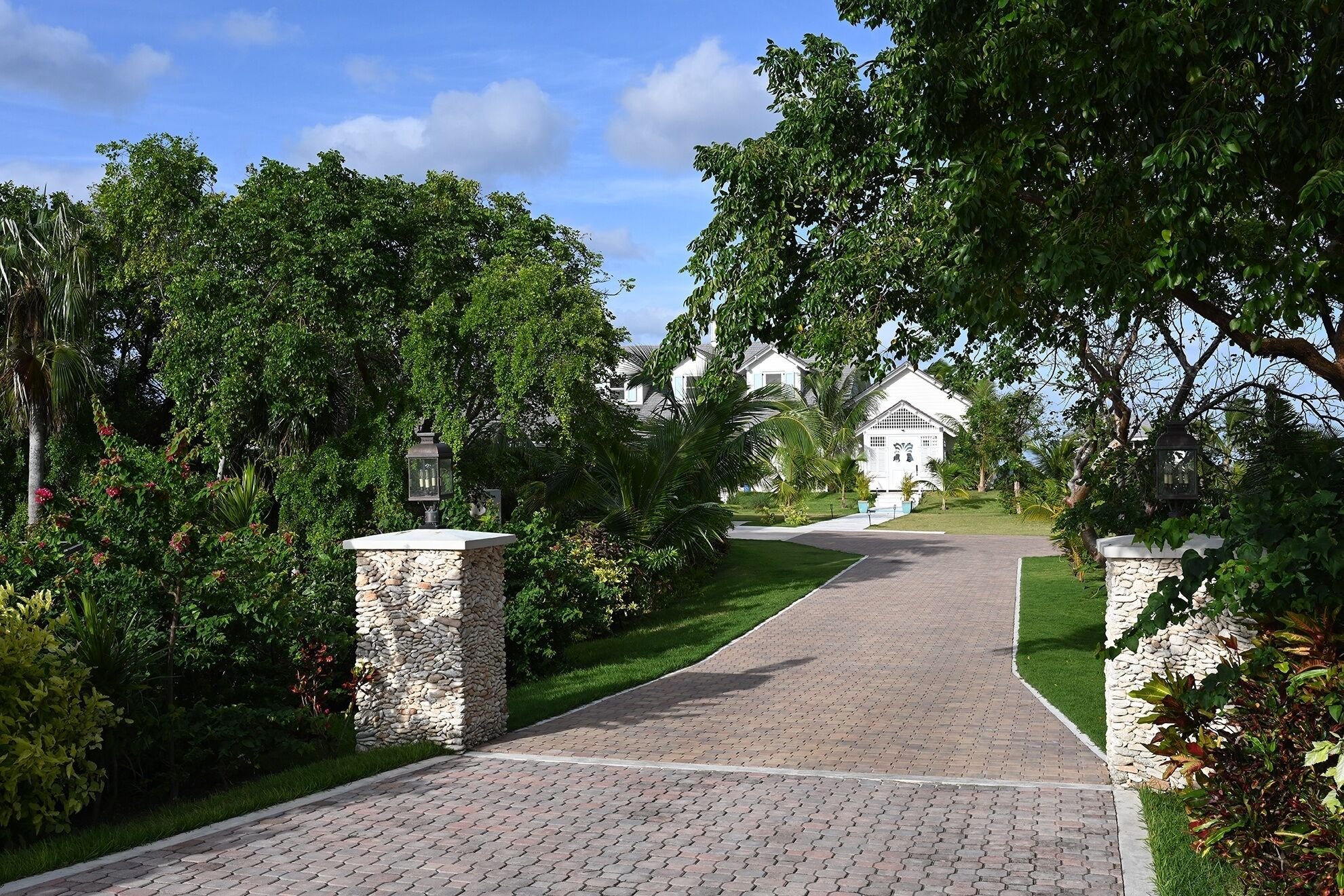 A paved pathway leading to a row of white buildings with a stone pillar on each side.