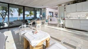 A modern kitchen with white cabinets, a dining area with a table and chairs, and a view of the ocean. - Hohum - Private Beachfront House On Exclusive Windermere 3 Bedroom Home (Savannah Sound)