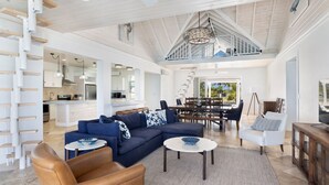 A spacious living area with a large sectional sofa, a brown leather chair, and a dining area with a high ceiling and natural light. - Buttonwood Reserve Compound - Compound W/beach, Pool, Pickleball 17 Bedroom Condo (James Cistern)