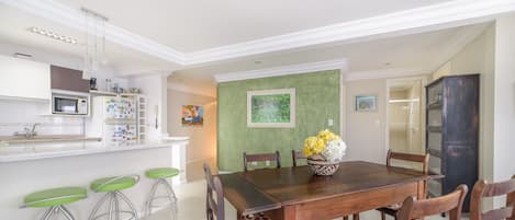A dining area with a wooden table, four chairs, a vase with flowers, and a green accent wall.