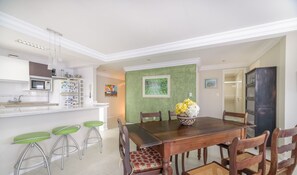 A dining area with a wooden table, four chairs, a vase with flowers, and a green accent wall. - 2BR Seafront apt W/garage in BC Nvi501 (Balneário Camboriú)