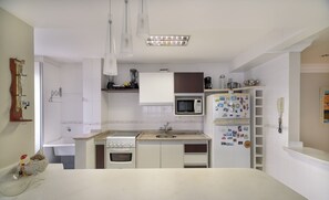 A compact kitchen with white cabinets, a built-in oven, a microwave, and a refrigerator with magnets.