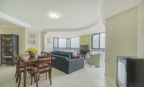 Amplia sala de estar con comedor, un conjunto de sofás, televisor y un ventanal con vistas.