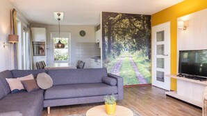 Een moderne woonkamer met een grijze bank, een gele plant en een televisie op een houten dressoir.