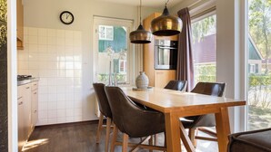 Een moderne keuken met witte tegels, een houten eettafel met vier stoelen, een klok aan de muur en een raam met gordijnen.