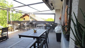 Un patio al aire libre con mesas y sillas, una planta en maceta y vista de un edificio al fondo.