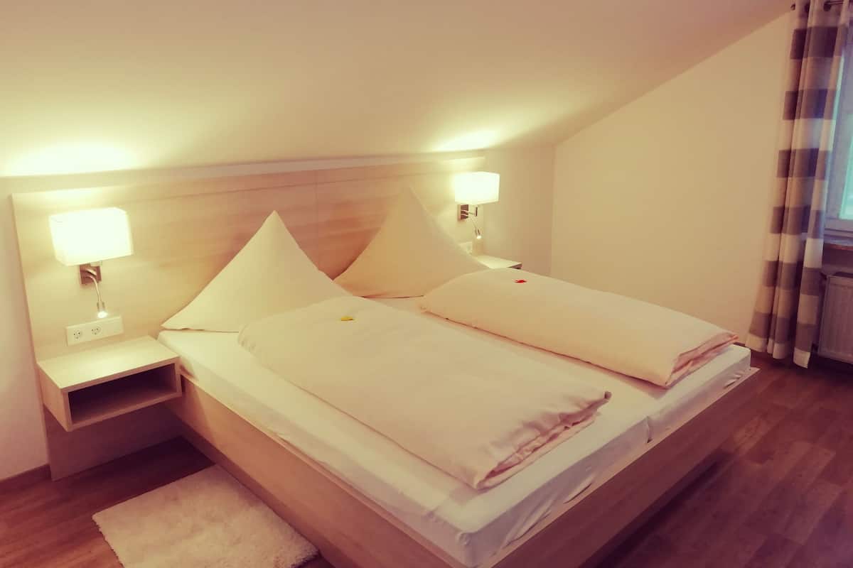 A hotel room with a single bed, two bedside lamps, a nightstand, and a window with curtains.