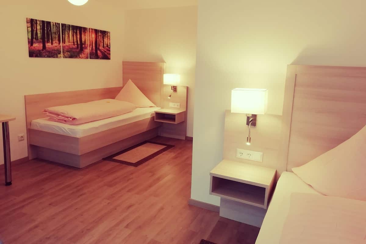 A neatly arranged hotel room with a bed, bedside tables, a wall-mounted lamp, and a painting of a forest scene.