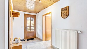 Um corredor com soalho de madeira, um radiador, um cabide e uma porta com janela.
