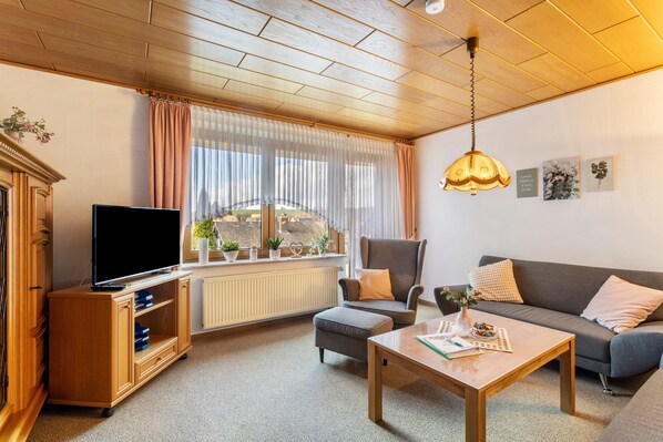 Sala de estar con televisión, sofá, sillón, mesa de centro y una ventana con cortinas.