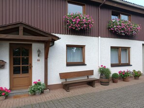 A building with a wooden door, windows, and a bench outside. - Apartment 'Tannenberg' with Shared Terrace, Private Garden and Wi-Fi (Diemelstadt)