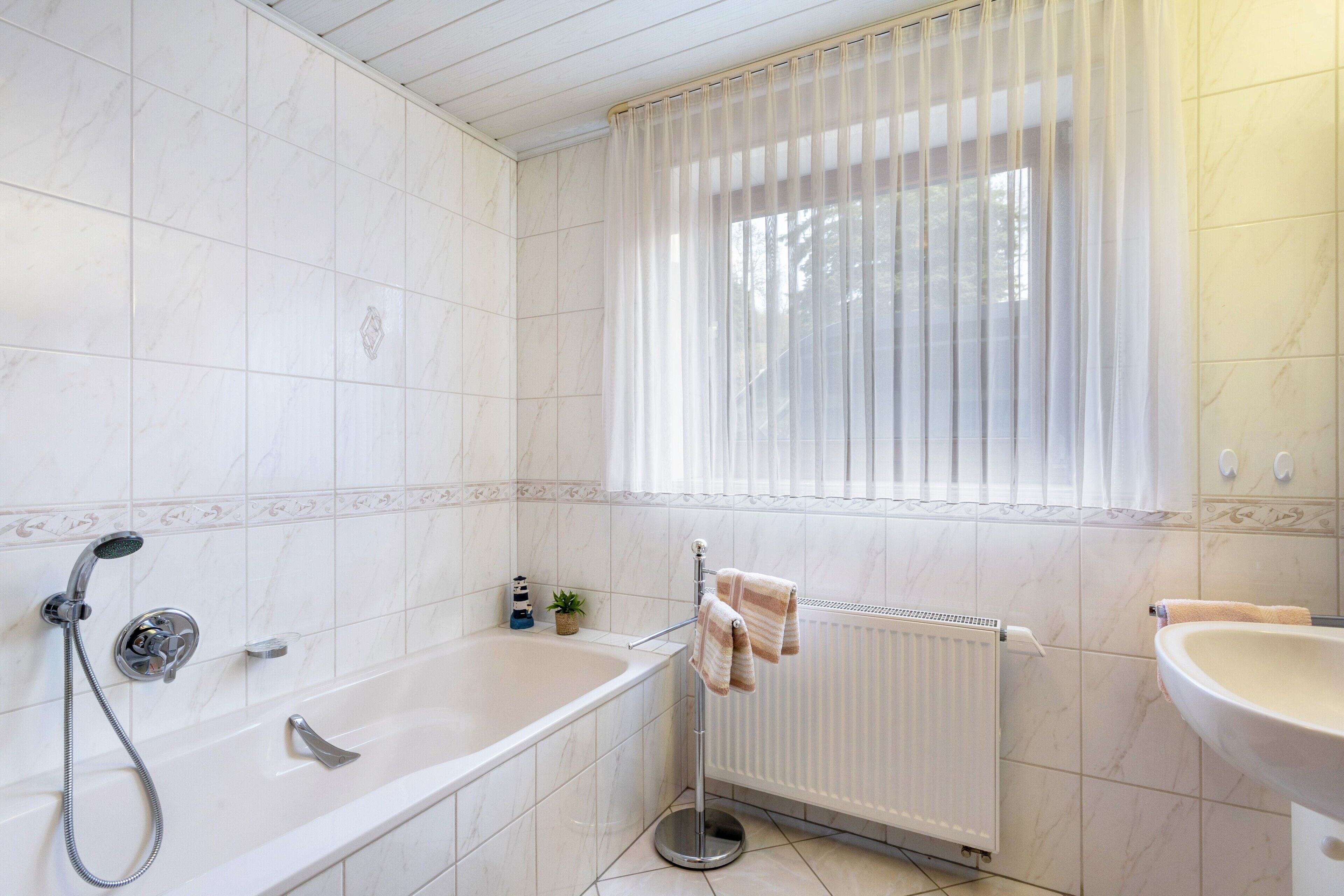 Un baño con bañera, ducha, ventana con cortinas y lavabo.