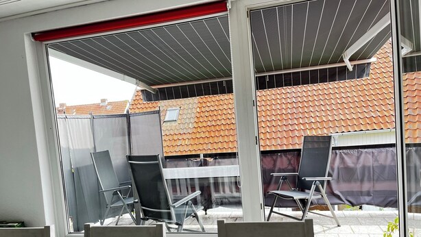 A patio area with a table and chairs, a covered seating area, and a view of a tiled roof building. - Modern vacation apartment with large balcony in Königslutter am Elm! Dogs welcome (Königslutter)