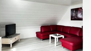 A modern living room with a red sectional sofa, a small white coffee table, and a television on a wooden stand. - Modern vacation apartment with large balcony in Königslutter am Elm! Dogs welcome (Königslutter)