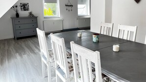 A dining area with a dark table, white chairs, and a small cabinet. - Modern vacation apartment with large balcony in Königslutter am Elm! Dogs welcome (Königslutter)
