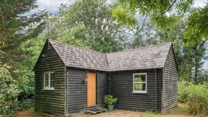 Une petite cabane en bois sombre, avec un toit en pente, une porte en bois et deux fenêtres.