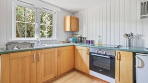 Une cuisine dotée de meubles en bois, d’un four Bosch, d’une fenêtre donnant sur la verdure et d’un plan de travail sur lequel sont disposés divers ustensiles de cuisine.