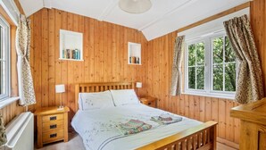 Une chambre à coucher aux murs lambrissés, avec un lit, des tables de chevet et une fenêtre avec des rideaux.