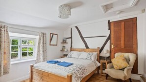 Ein Schlafzimmer mit einem hölzernen Bett, einem Sessel, einem Fenster mit Vorhängen und einer Holztür.
