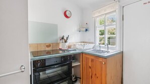 Eine kompakte Küche mit Herd, Backofen, Spüle und einem Fenster mit Blick ins Grüne.