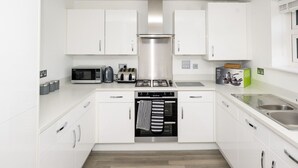 A modern kitchen with white cabinets, a stainless steel range hood, a microwave, toaster, and oven.