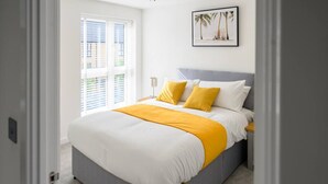 A bedroom with a bed, a nightstand, a framed picture on the wall, and a window with blinds.