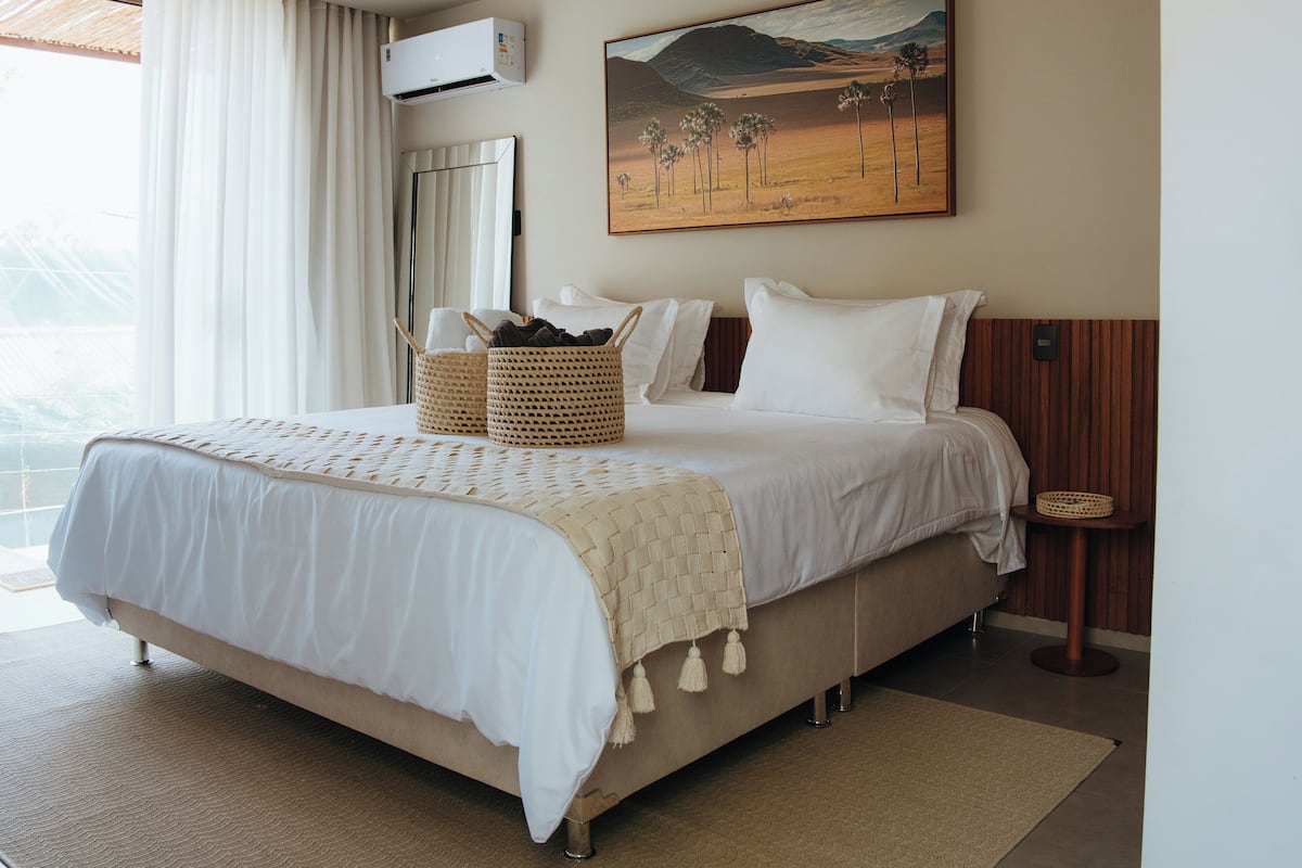 A bedroom with a large bed, a painting on the wall, and an air conditioning unit.