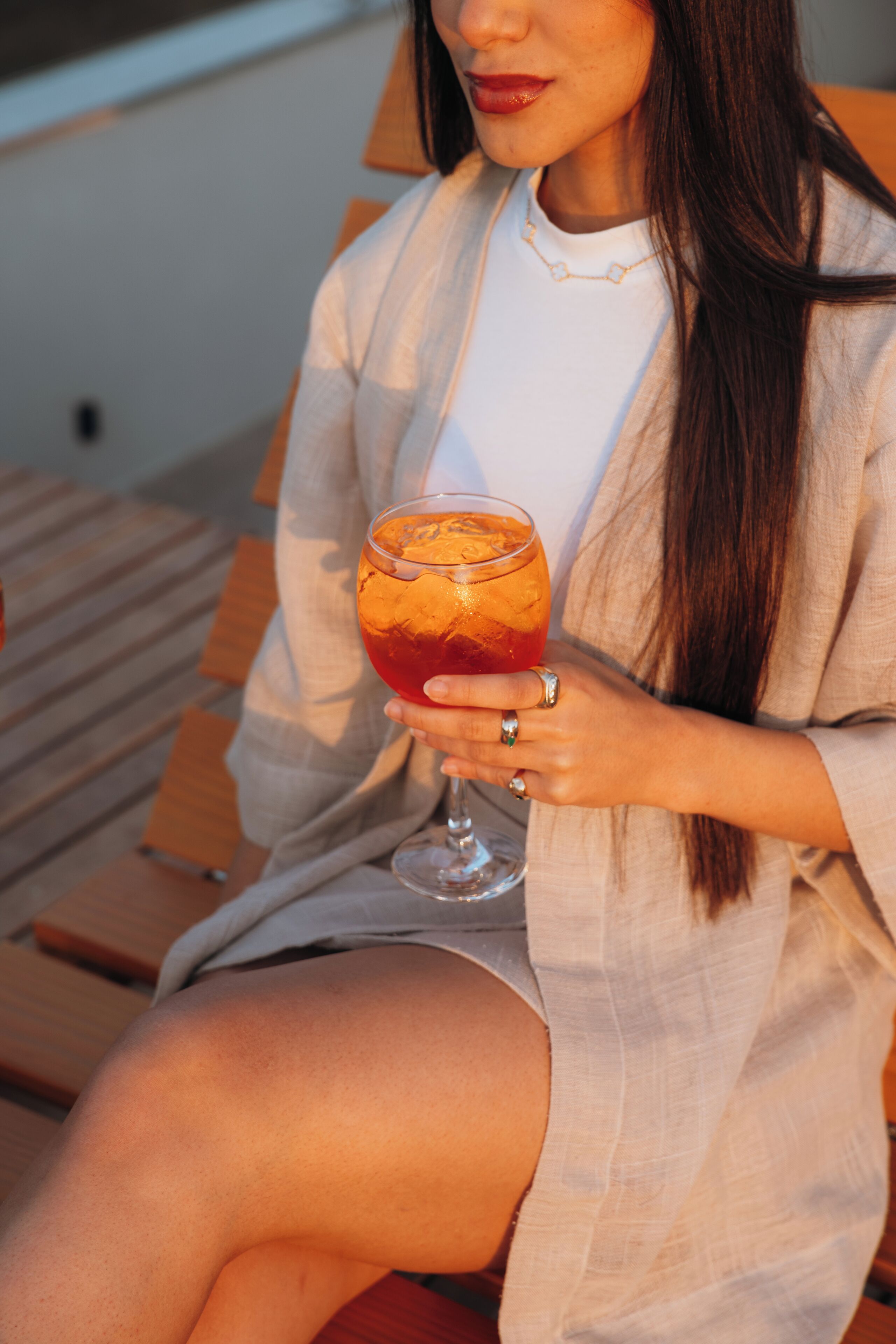 A person sitting on a wooden bench holding a glass of drink.