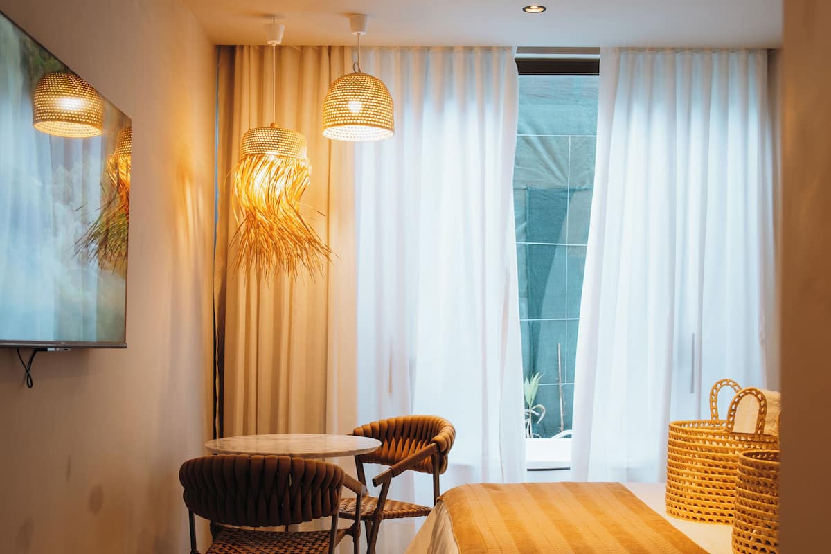 A hotel room with a bed, a round table with chairs, a TV mounted on the wall, and a large window with curtains.