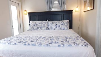 Uma cama com colcha florida, cabeceira escura e duas luminárias fixadas na parede.