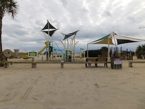 A playground with various play structures, a bench, and a sign indicating beach parking rules.
