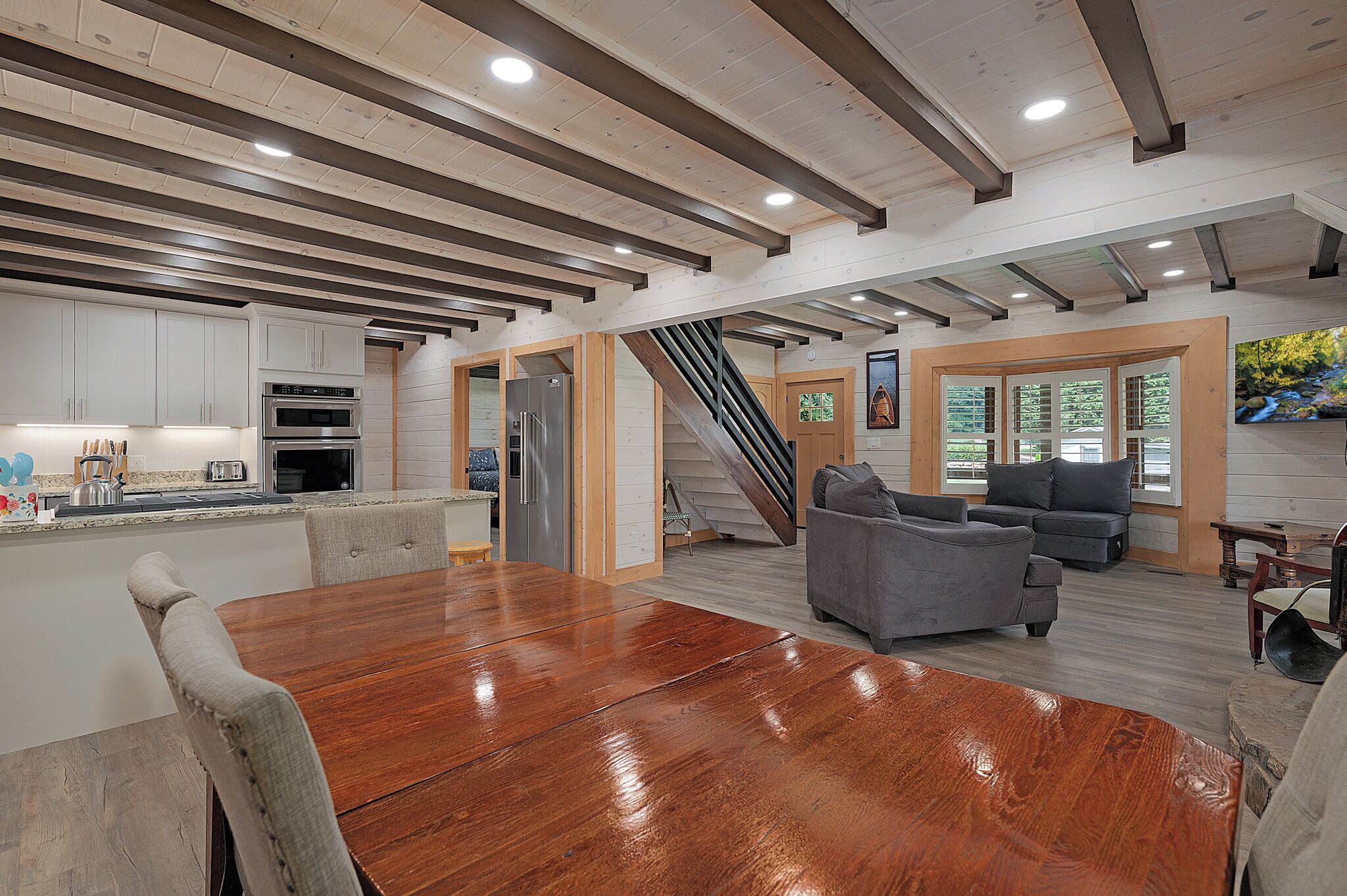 A spacious living area with a wooden dining table, grey sofas, and a staircase leading to another level.