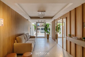 A modern hotel lobby with a sofa, seating area, potted plants, and a chandelier. - OBP \- Condomínio Moderno a 600m da Praia (Penha)