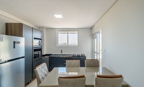 A modern kitchen with a dining area, featuring a built-in oven, microwave, and gas stove. - OBP \- Condomínio Moderno a 600m da Praia (Penha)