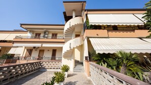 Um edifício com vários andares, uma escadaria em espiral, área de estar externa e uma palmeira.