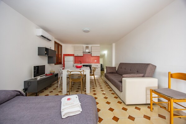 Ein kompaktes Hotelzimmer mit Bett, Sofa, Esstisch mit Stühlen, Fernseher und Küchenzeile.