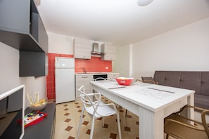 A modern kitchen with a dining area, white cabinetry, a red backsplash, and a grey sofa. - Apartment 'Casa Artale' with Shared Terrace and Air Conditioning (Capo d'Orlando)