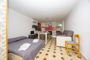 Ein kleines Hotelzimmer mit Bett, Sessel, Tisch, einer Küchenzeile und einem Badezimmer.