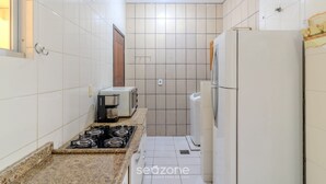 Una cucina compatta con piastrelle bianche, un fornello a gas, un frigorifero e un forno a microonde.