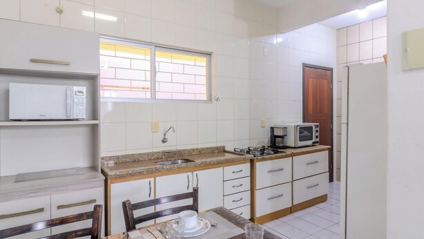 Una cucina compatta con mobili bianchi, un forno a microonde, un piano cottura a gas e una finestra con inferriate.