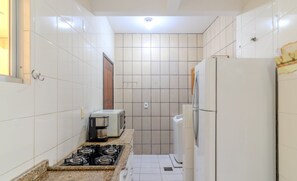 Cocina compacta con baldosas blancas, estufa a gas, refrigerador y microondas.