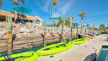 A dock with kayaks, a pool, and a thatched-roof structure.